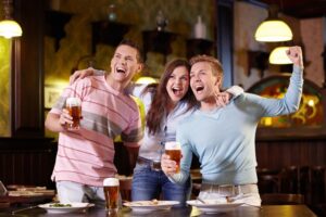 Three people cheering and drinking beer at a sports bar.